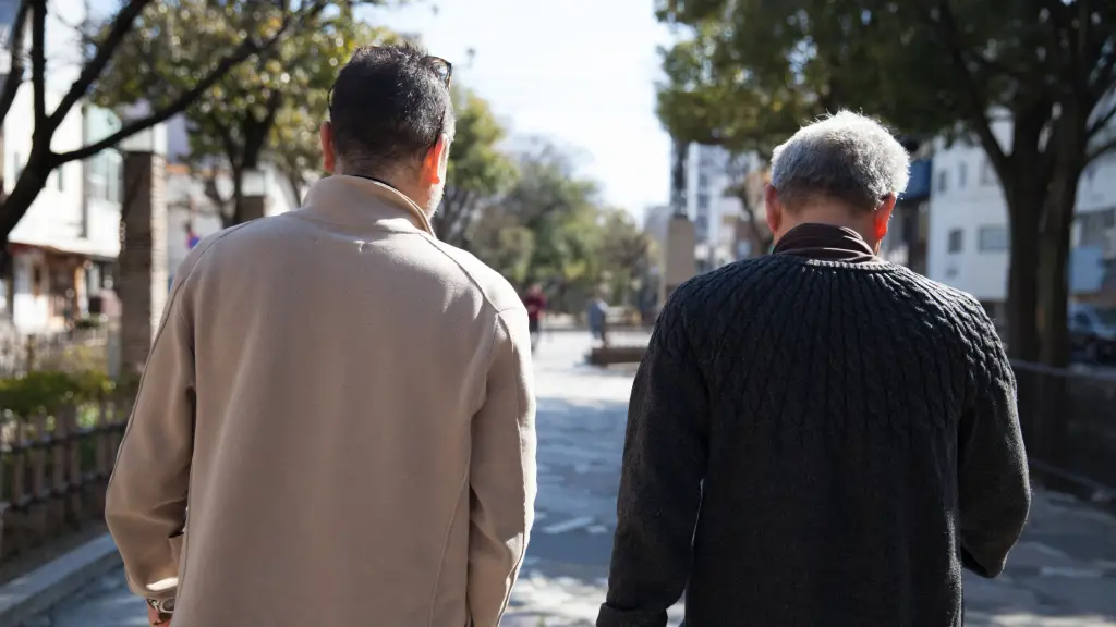 Two men are walking beside each other, facing away from the camera. One is older.