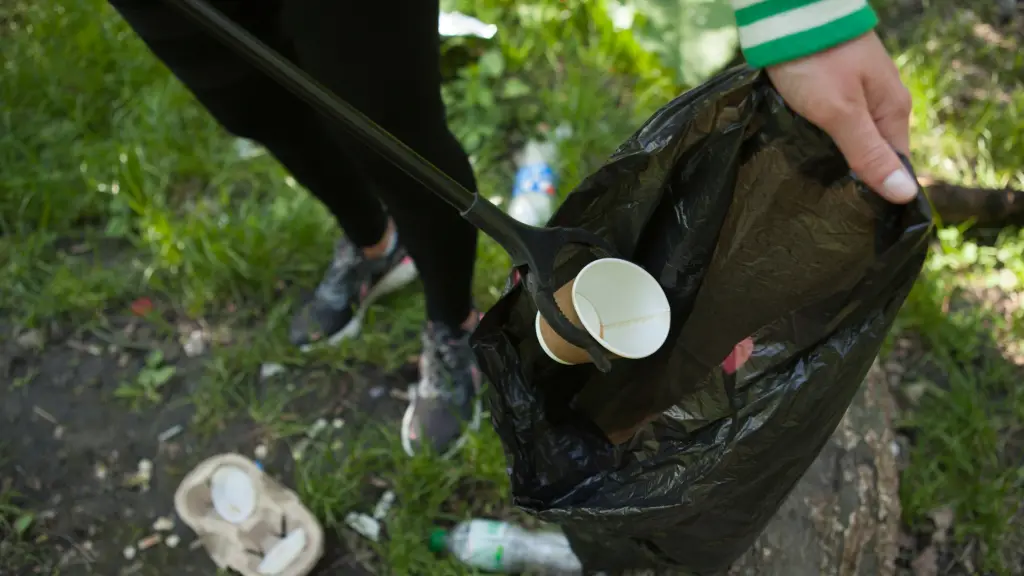 A person puts a cardboard coffee cup into a rubbish bag using a litter pick tool.